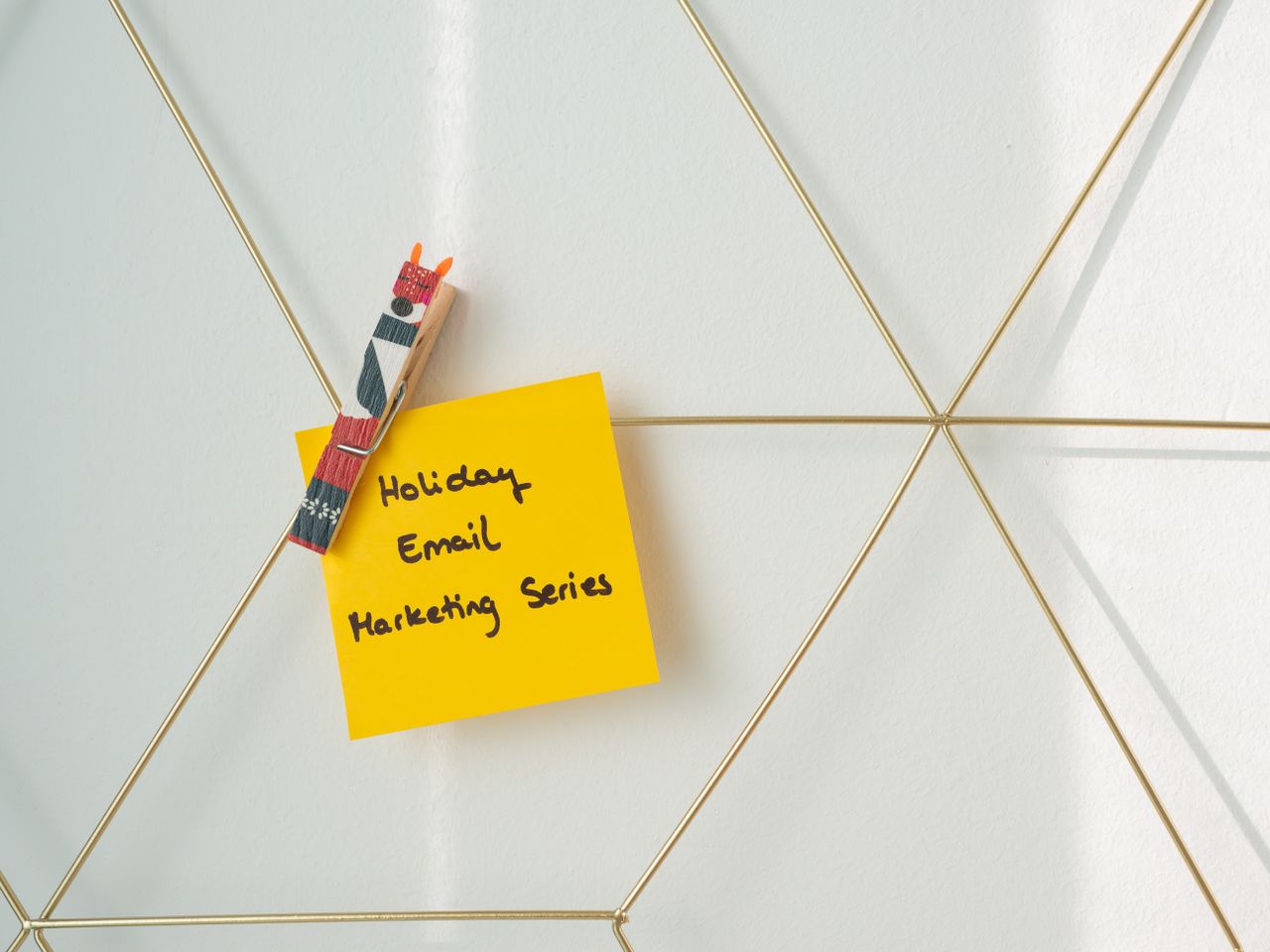 A bright yellow sticky note pinned to a wireframe wall, carrying a holiday email marketing message.